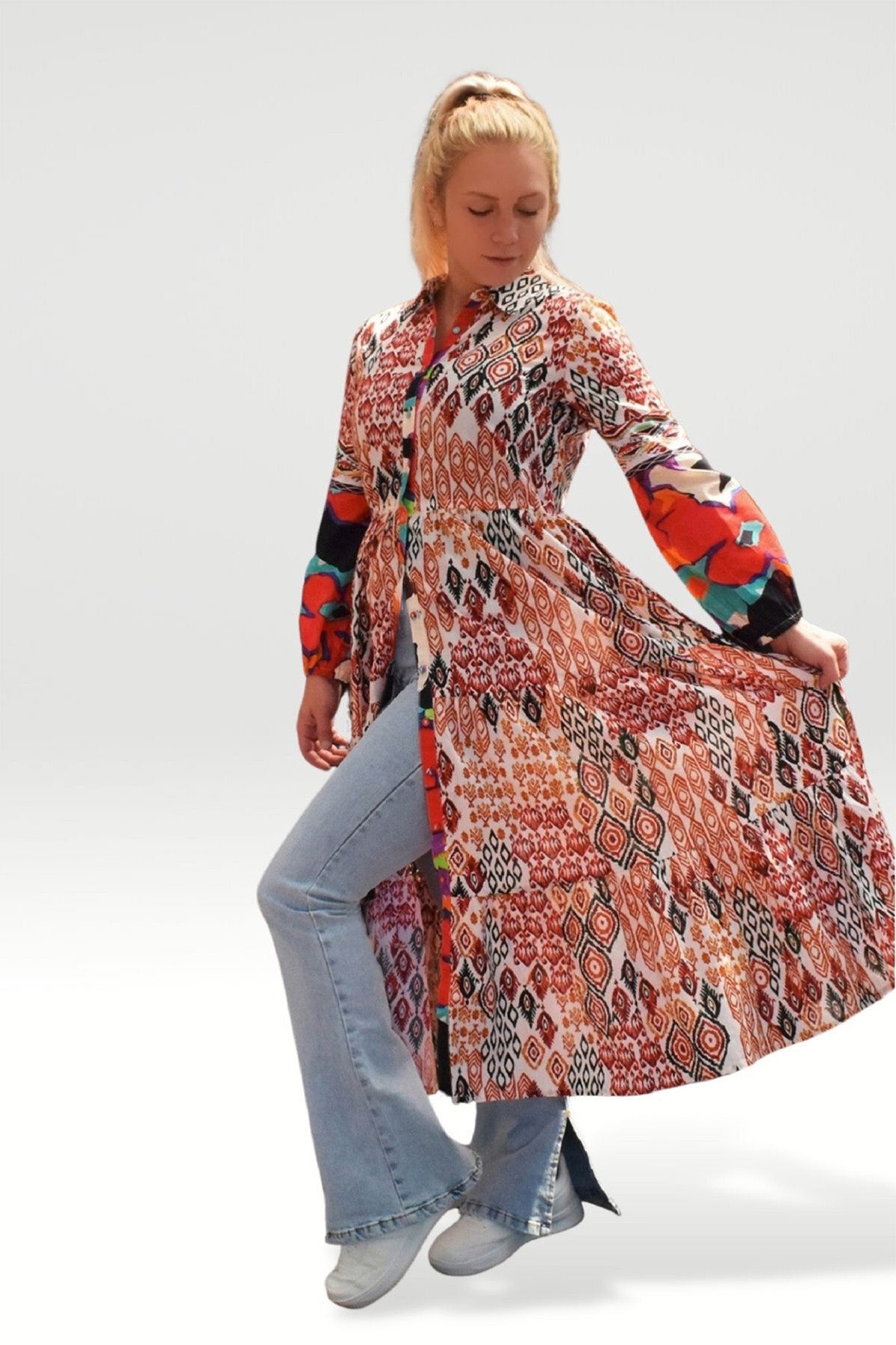 MODEL WITH BLONDE HAIR WEARING TOZI PRINTED TIER MAXI DRESS OVER JEANS  AND WHITE SNEAKERS- zohaonline